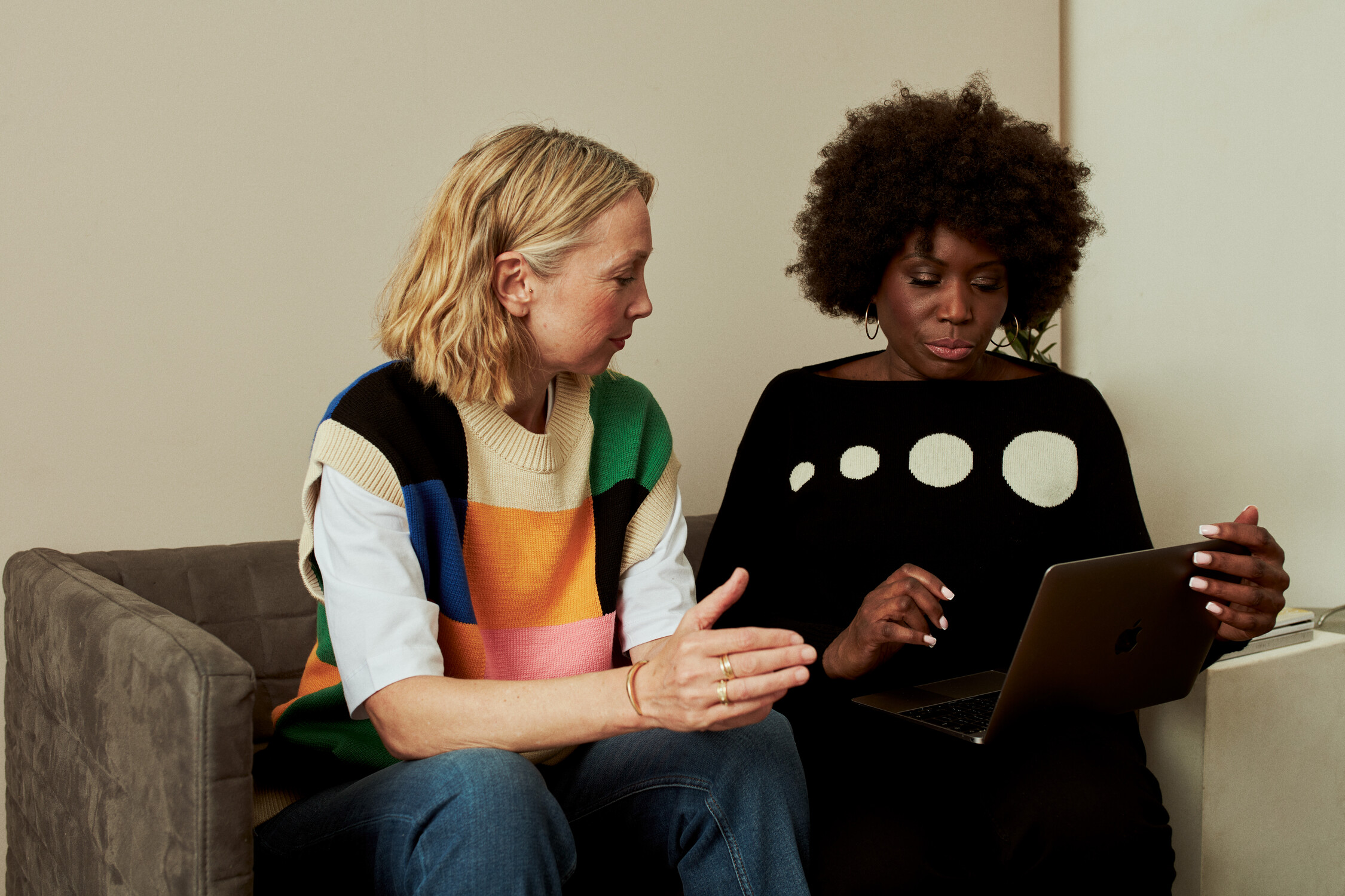 Two women, one white one black fill in an application form for a grant on an iPad. They are sitting on a sofa.