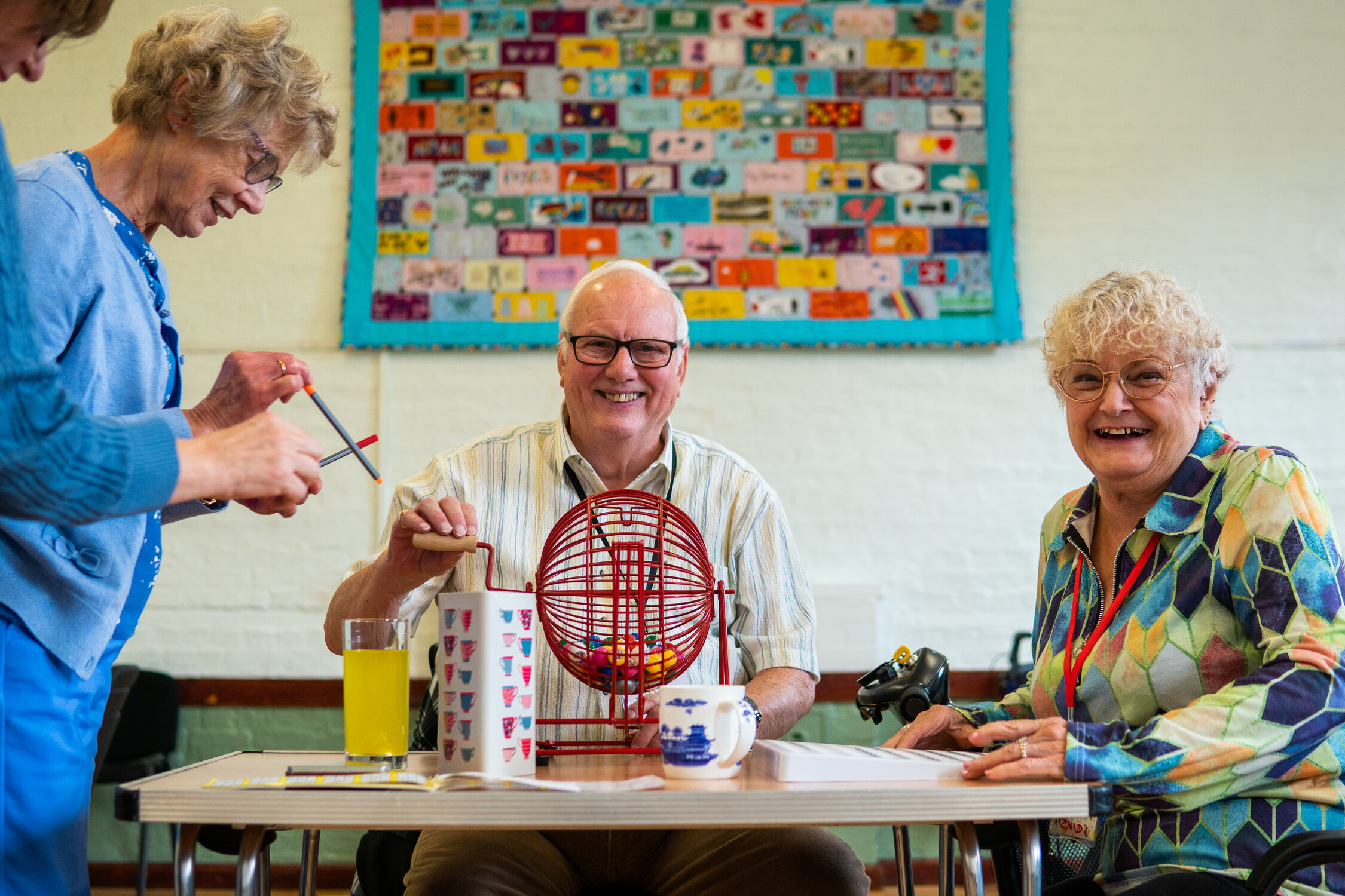 Three older people play bingo in a community centre. They are happy.