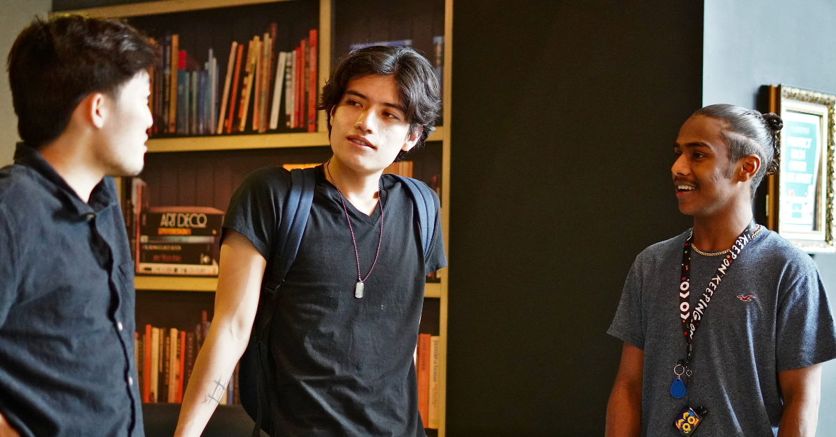 Three students chat casually in a library
