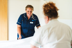 Two nurses change a bed. One wears blue one wears white.