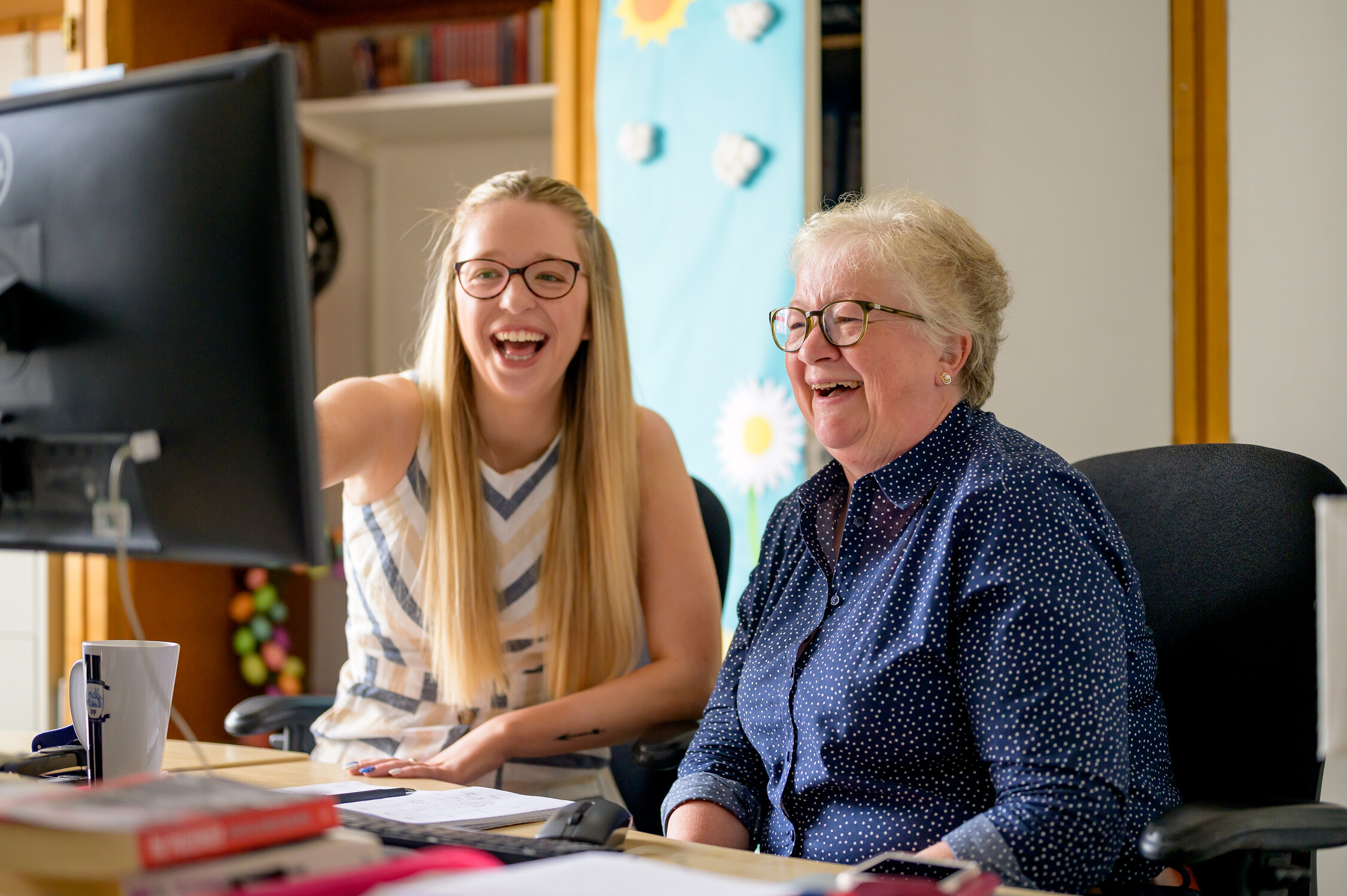 Two women look at a computer screen and laugh