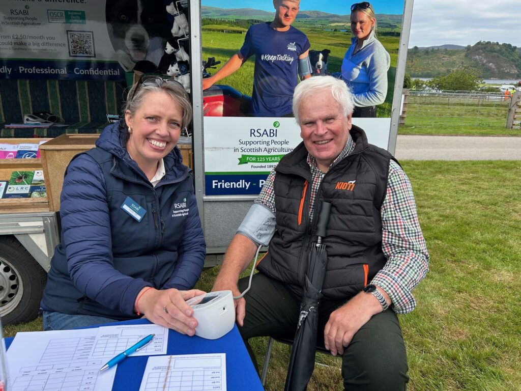 A man with white hair and a checked shirt has his blood pressure checked by a nurse outside at an agricultural show.