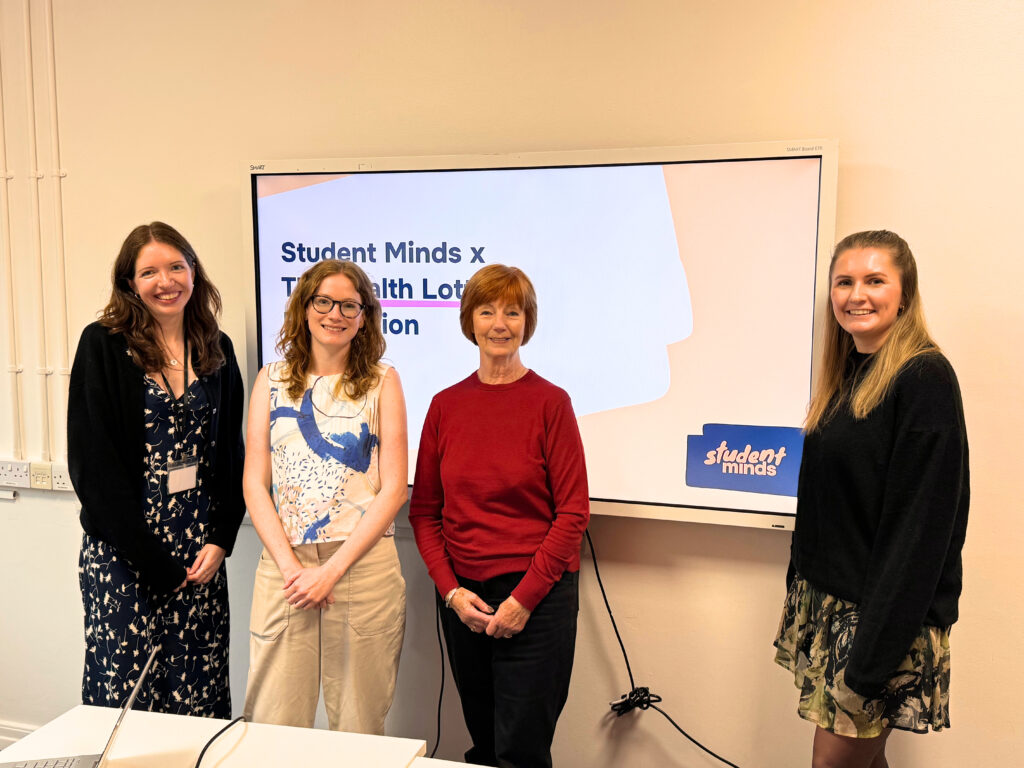 Four women stand in front of a presentation screen in a classroom. It says student minds on the screen.