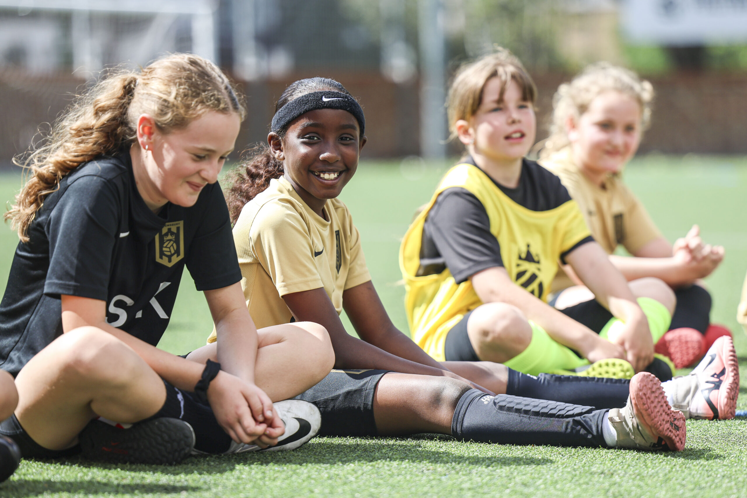 4 girls in football kit sit on the floor at Bloomsbury Football Foundation