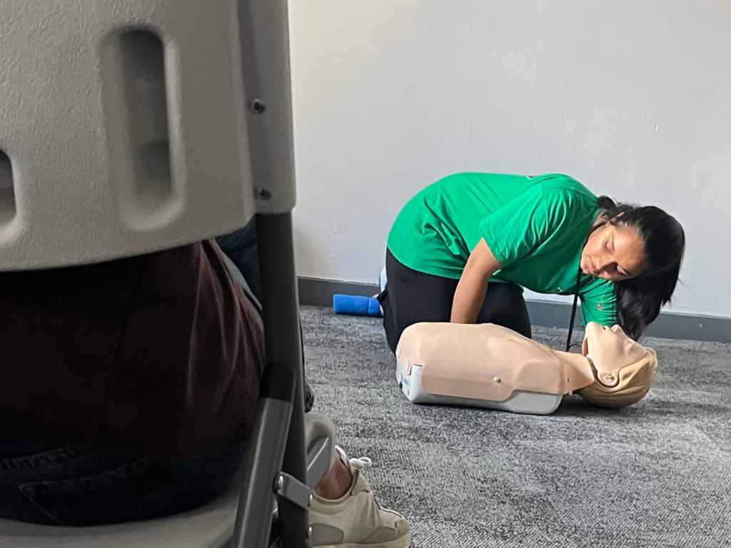 A woman in a green shirt works on a resuscitation dummy